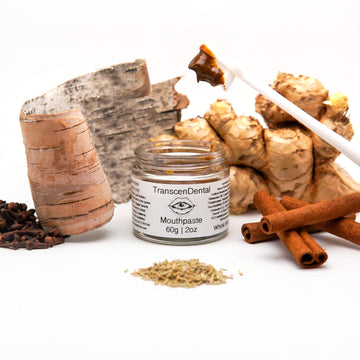 Open jar of TranscenDental toothpaste for receding gums with a toothbrush and botanicals