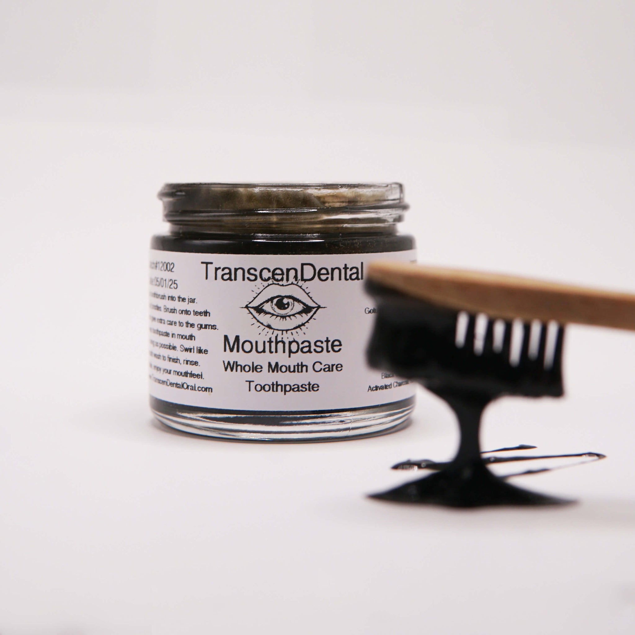 charcoal toothbrush with toothpaste and organic xylitol toothpaste dripping off into jar of baking soda toothpaste. 