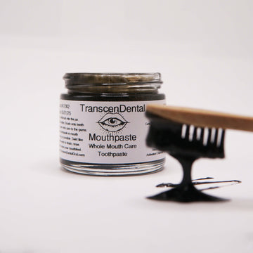 charcoal toothbrush with toothpaste and organic xylitol toothpaste dripping off into jar of baking soda toothpaste. 