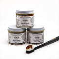Stack of three 60g jars of fluoride-free TranscenDental toothpaste with a toothbrush